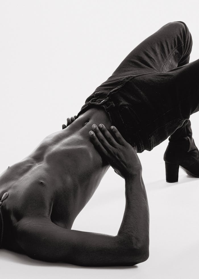 footer-01 An African American male model poses artistically wearing jeans and heels in a studio setting.