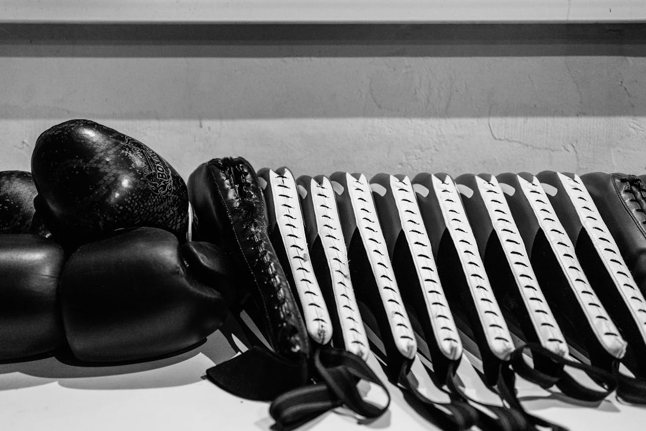 home-hero-02 Monochrome photo of boxing gloves and focus mitts in an indoor gym setting.